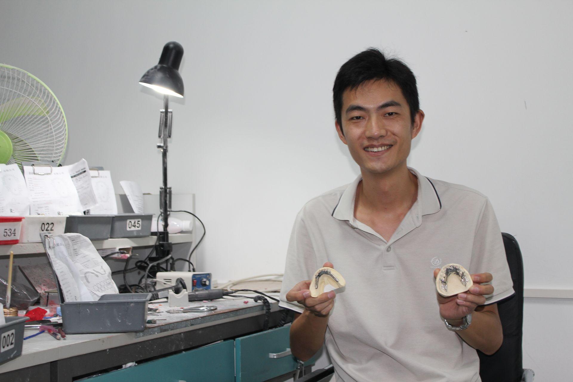 Person holding dental molds in a workshop with various tools and papers on the desk.