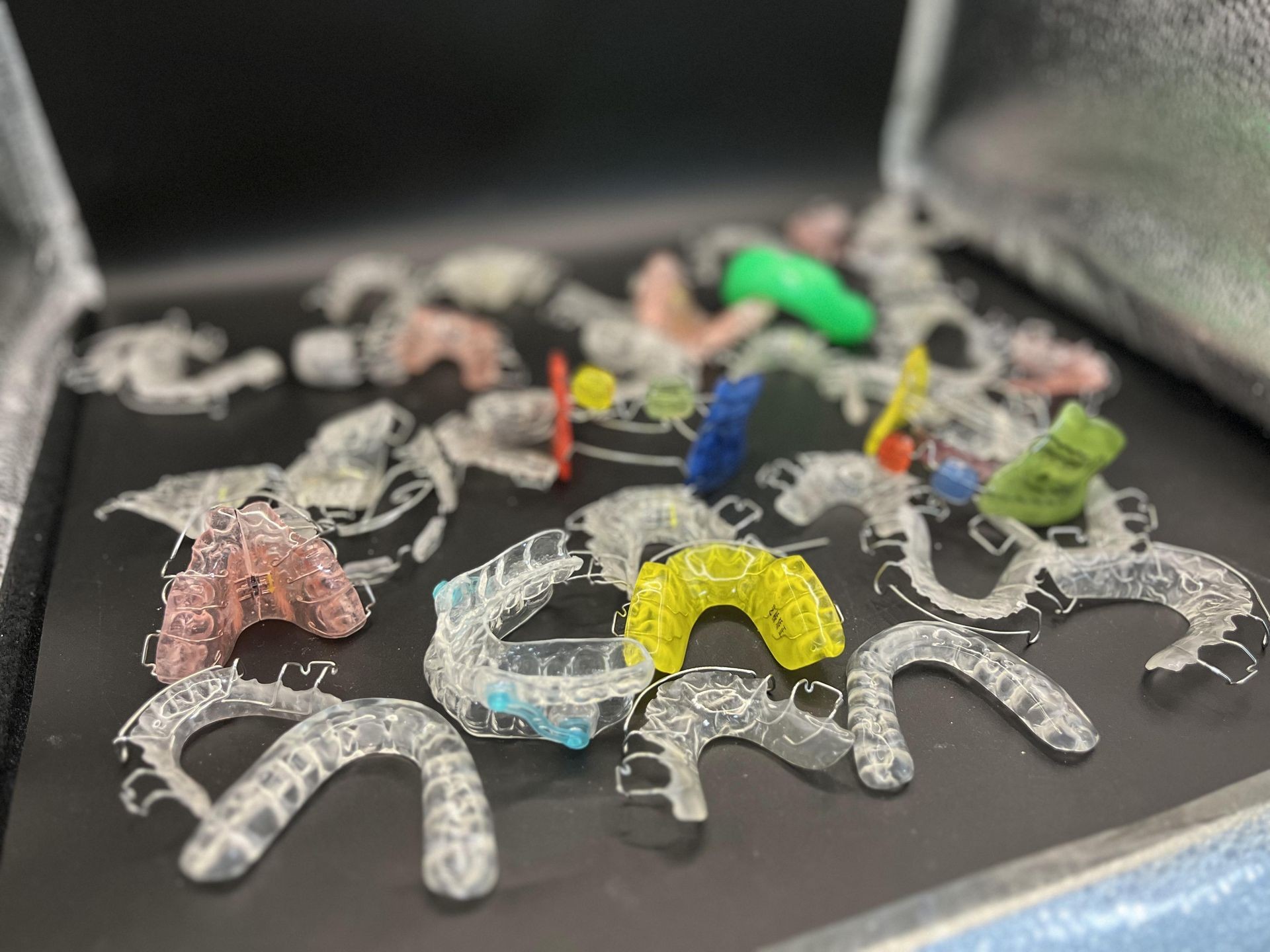 Various colored dental retainers scattered on a black tray.