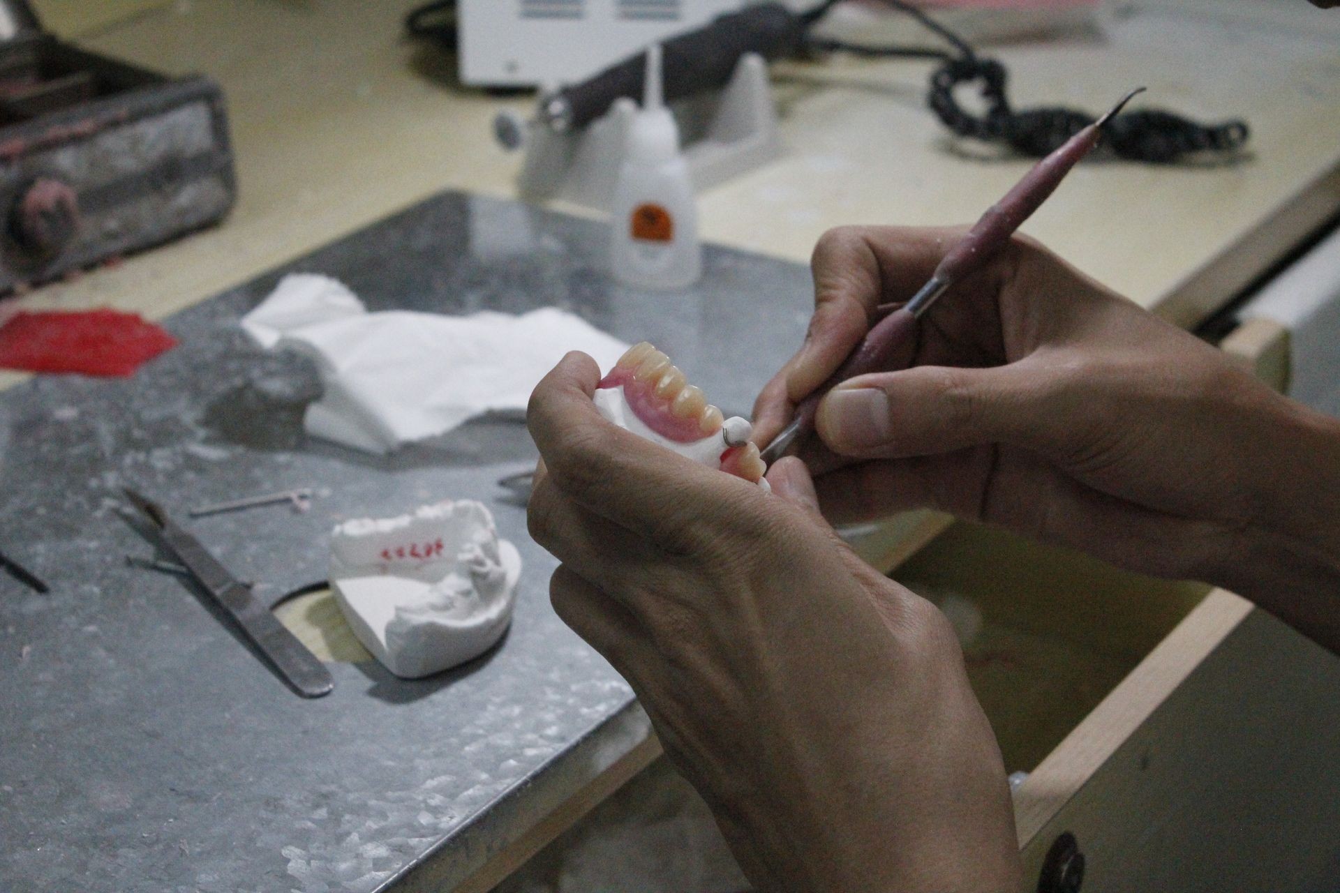 Technician working on a dental prosthesis at a workbench with various dental tools and materials.